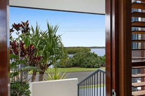 Blick von einem Balkon mit Geländer auf ein Gewässer und Grünflächen.