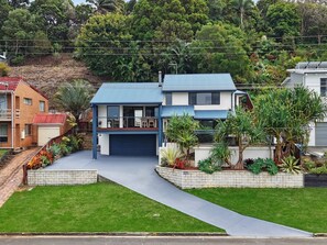 Ein modernes, zweistöckiges Haus mit Garage, umgeben von gepflegten Gärten und einer hügeligen Landschaft.