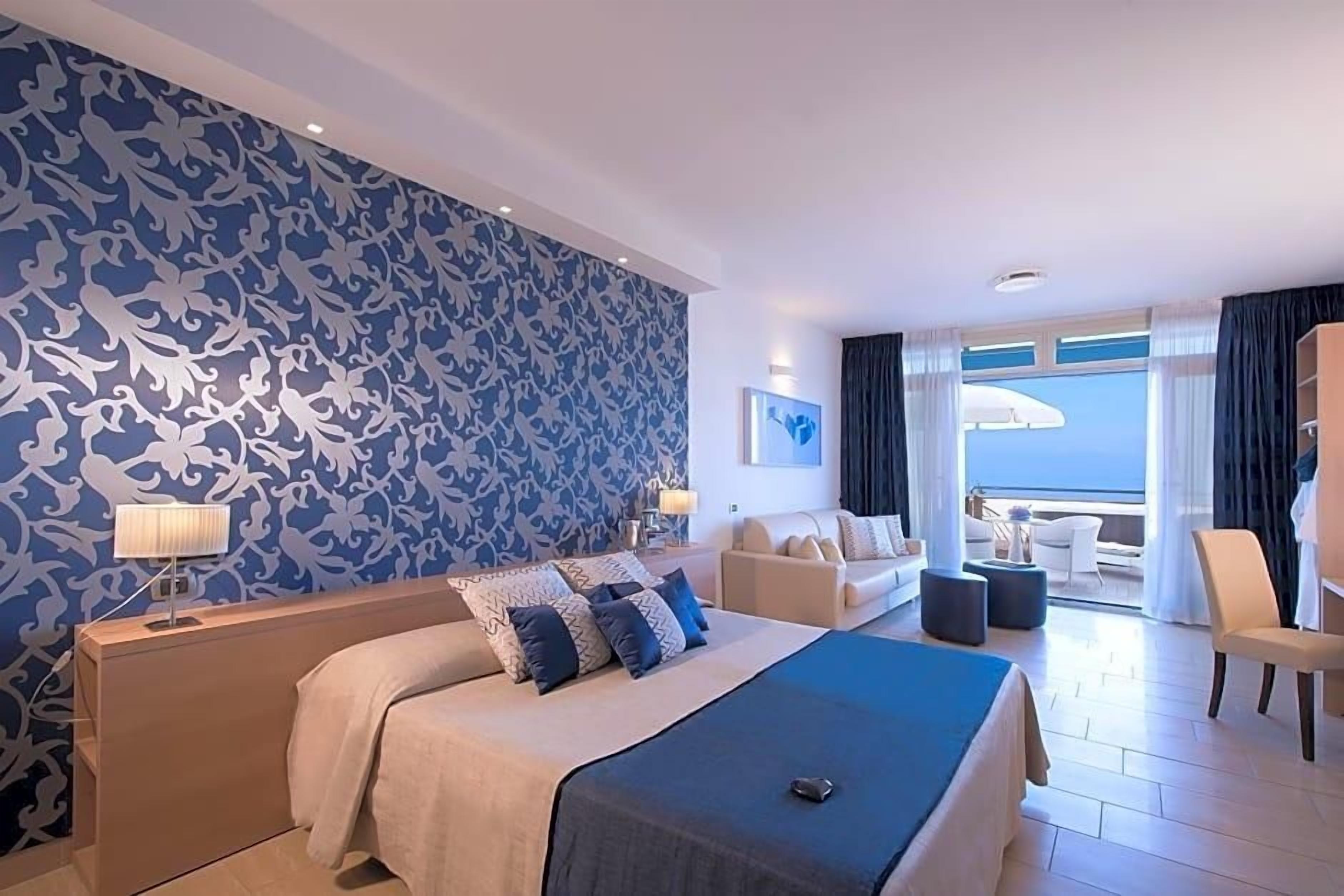 Una camera d'albergo con un letto grande, un divano, un balcone con vista e una parete decorata.