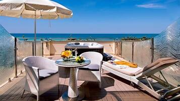 Una terrazza esterna illuminata dal sole con un tavolo, due sedie, una poltrona relax e un ombrellone grande.