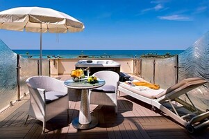 A sunlit outdoor deck with a table, two chairs, a lounge chair, and a large umbrella.