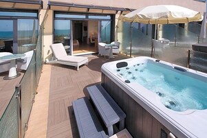A rooftop deck with a hot tub, lounge chairs, and a glass-enclosed area with a view of the sea.