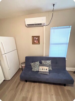 A compact living space with a blue sofa, a white refrigerator, and an air conditioning unit mounted on the wall. - 2 BR APT close to Ybor , airport, downtown, Busch Gardens & Adventure Island (Tampa)