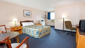 Et hotelværelse med seng, skrivebord, stol, fjernsyn og lampe.