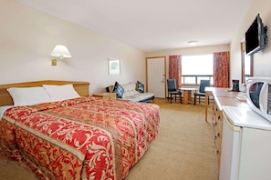 Een hotelkamer met een bed, een bureau, een stoel, een televisie en een raam met gordijnen.