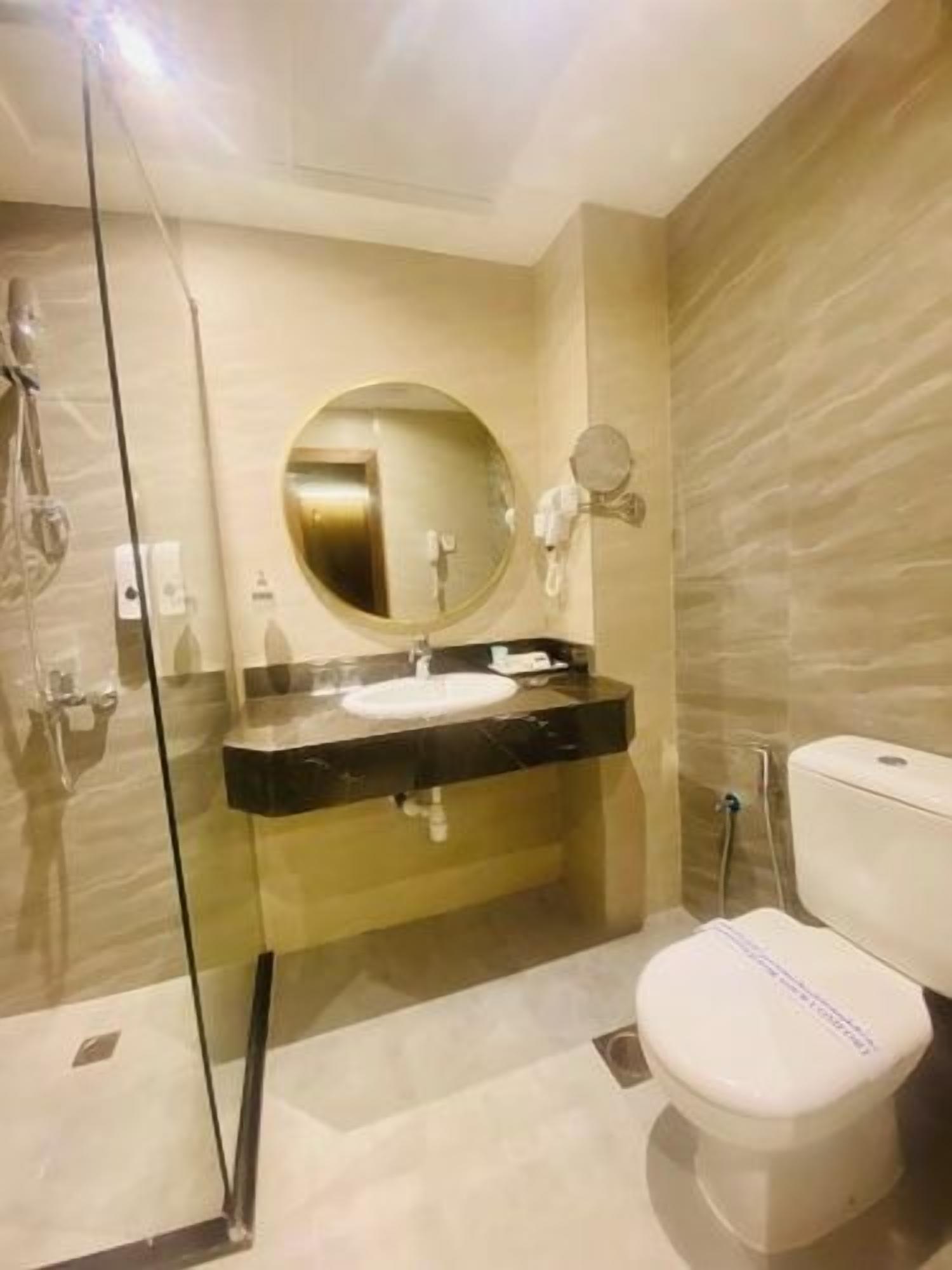 Een moderne badkamer met een glazen douchecabine, een ronde spiegel, een zwart aanrecht en een wit toilet.
