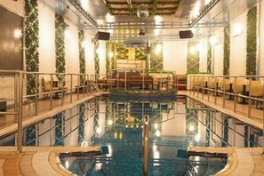 Ein Innenpool mit Sprungturm in der Mitte, umgeben von Sitzbereichen und einer Decke mit eingelassener Beleuchtung.