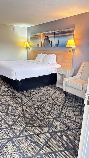 Une chambre d’hôtel avec un lit, une chaise, un bureau et une lampe fixée au mur.