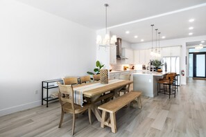 A modern kitchen with a central island, wooden dining table, and bar stools. - Sunset Shores Retreat | 3BR River-View Condo w/ Double Balcony & Private Beach Access (Melbourne Beach)