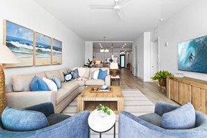 A modern living room with a sectional sofa, a coffee table, and a TV on a wooden cabinet. - Sunset Shores Retreat | 3BR River-View Condo w/ Double Balcony & Private Beach Access (Melbourne Beach)