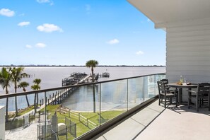 A balcony with a view of a marina, outdoor seating, and a palm tree. - Sunset Shores Retreat | 3BR River-View Condo w/ Double Balcony & Private Beach Access (Melbourne Beach)