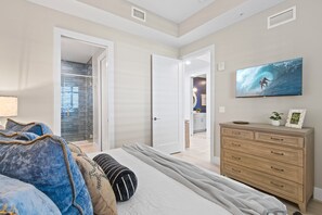 A bedroom with a bed, a dresser, and a TV on the wall. - Sunset Shores Retreat | 3BR River-View Condo w/ Double Balcony & Private Beach Access (Melbourne Beach)