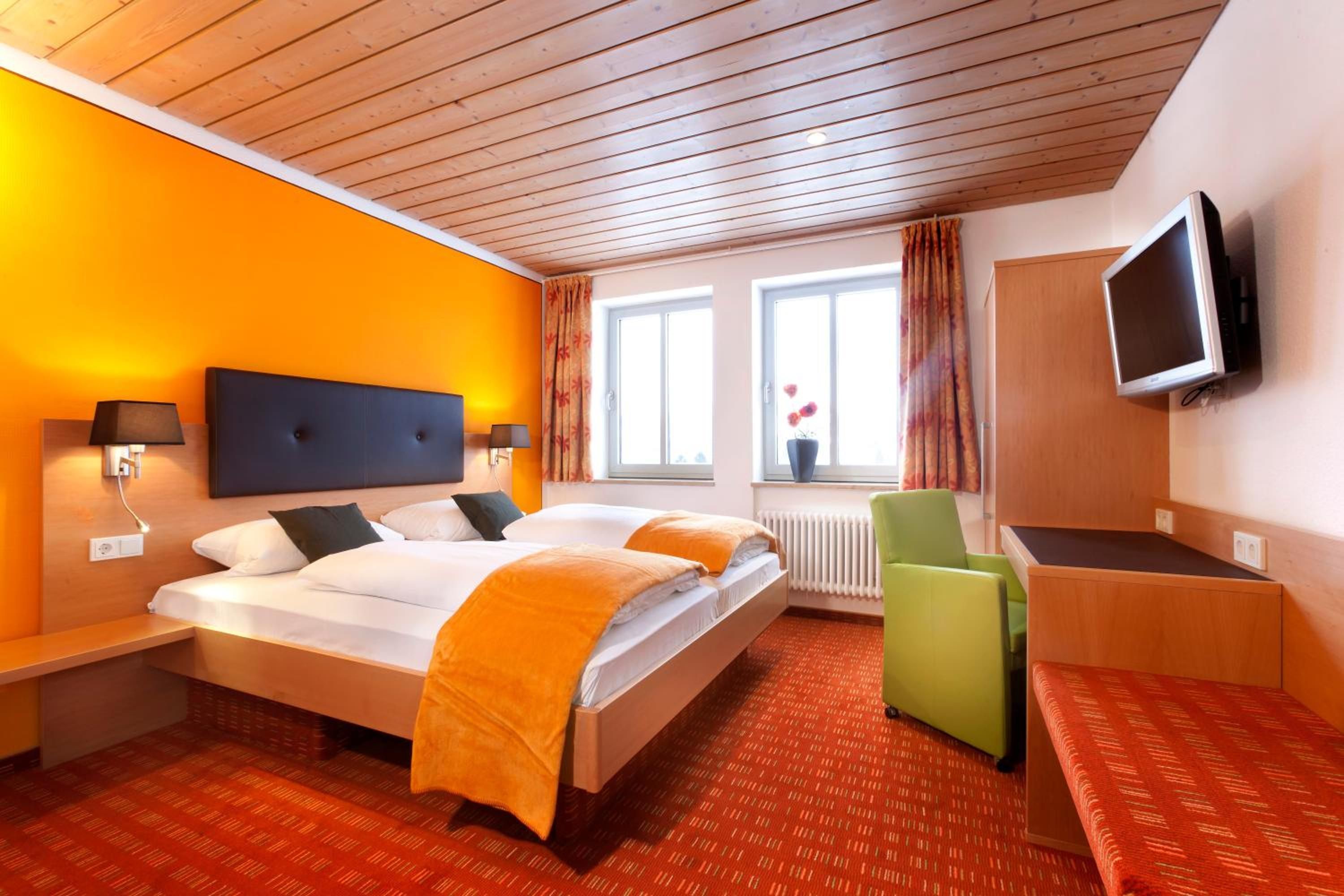 Ein Hotelzimmer mit einem Bett, Nachttischen, einem Schreibtisch, einem Sessel, einem Fernseher und einem fenster mit Vorhängen.