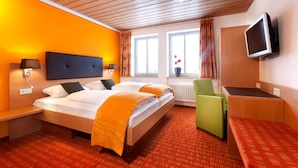 A hotel room with a bed, bedside tables, a desk, a chair, a television, and a window with curtains. - Waldhorn (Kempten)