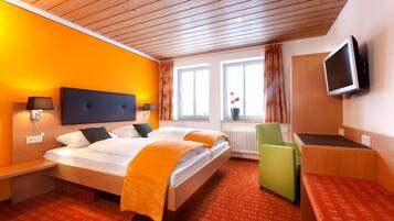 Ein Hotelzimmer mit einem Bett, Nachttischen, einem Schreibtisch, einem Sessel, einem Fernseher und einem fenster mit Vorhängen.
