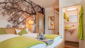 A hotel room with two beds, a large window with a tree view, a bathroom with a sink and mirror, and a door leading to another room. - Waldhorn (Kempten)