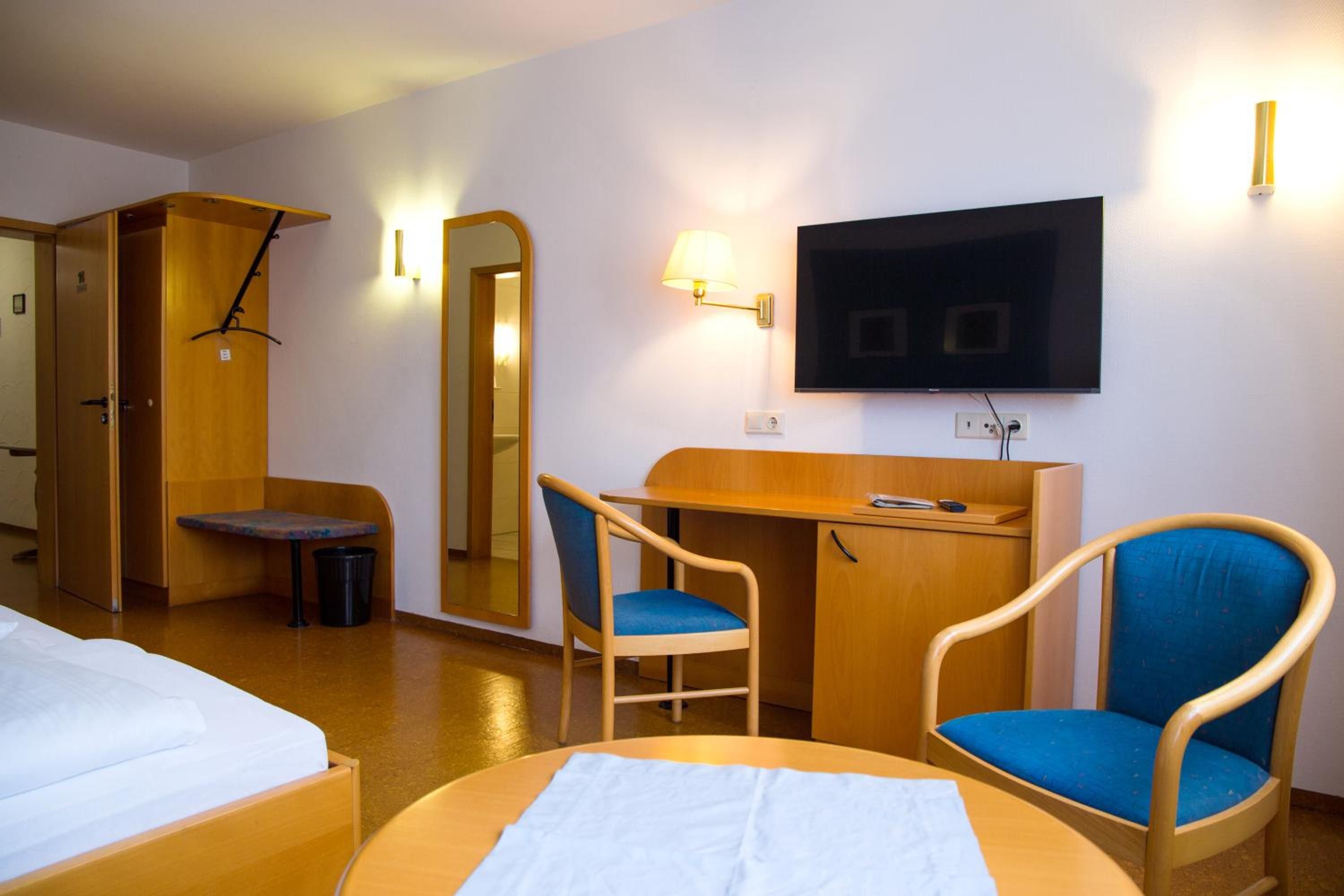 A hotel room with a bed, a desk, two chairs, a television, and a mirror.