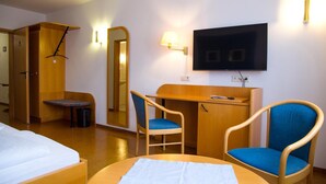 Een hotelkamer met een bed, een bureau, twee stoelen, een televisie en een spiegel.