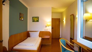A hotel room with a bed, a chair, a desk, a mirror, and a door.