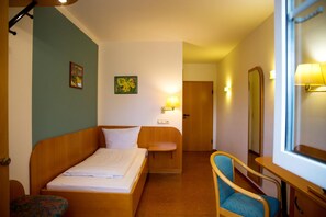Quarto de hotel com uma cama, uma cadeira, uma escrivaninha, um espelho e uma porta.