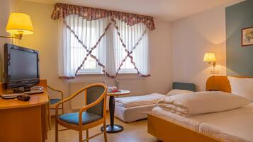 A hotel room with a desk, a television, a chair, a bed, and two bedside lamps.
