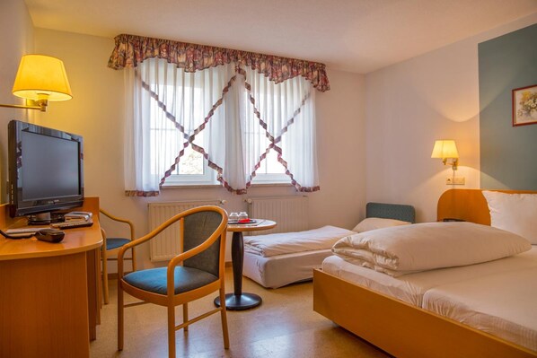Quarto de hotel com escrivaninha, televisão, cadeira, cama e duas luminárias de cabeceira.