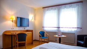 Een hotelkamer met een bed, een bureau, een stoel, een televisie en een raam met gordijnen.