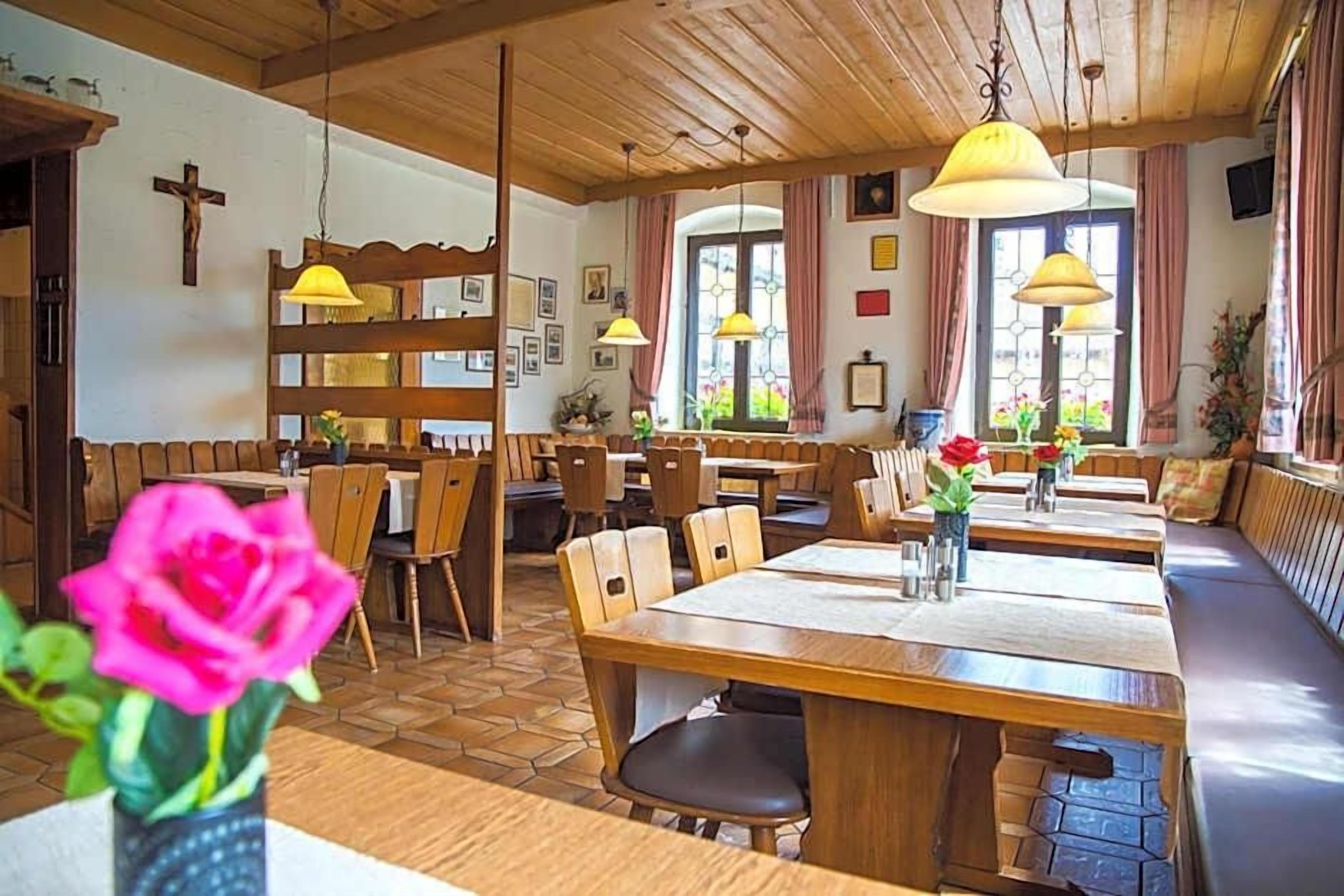 A restaurant with wooden tables and benches, a cross on the wall, and a window with curtains.