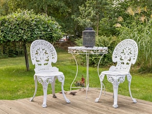 Two ornate white chairs with intricate designs, a small round table, and a decorative lantern on a wooden deck surrounded by lush greenery. - "Ølvir" - 525m from the sea by Interhome (Nykøbing Sj)