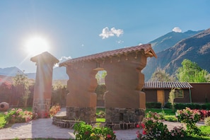 A traditional stone structure with a tiled roof, surrounded by a garden with various flowering plants. - CCAYPA Willka Qhichwa (Calca)