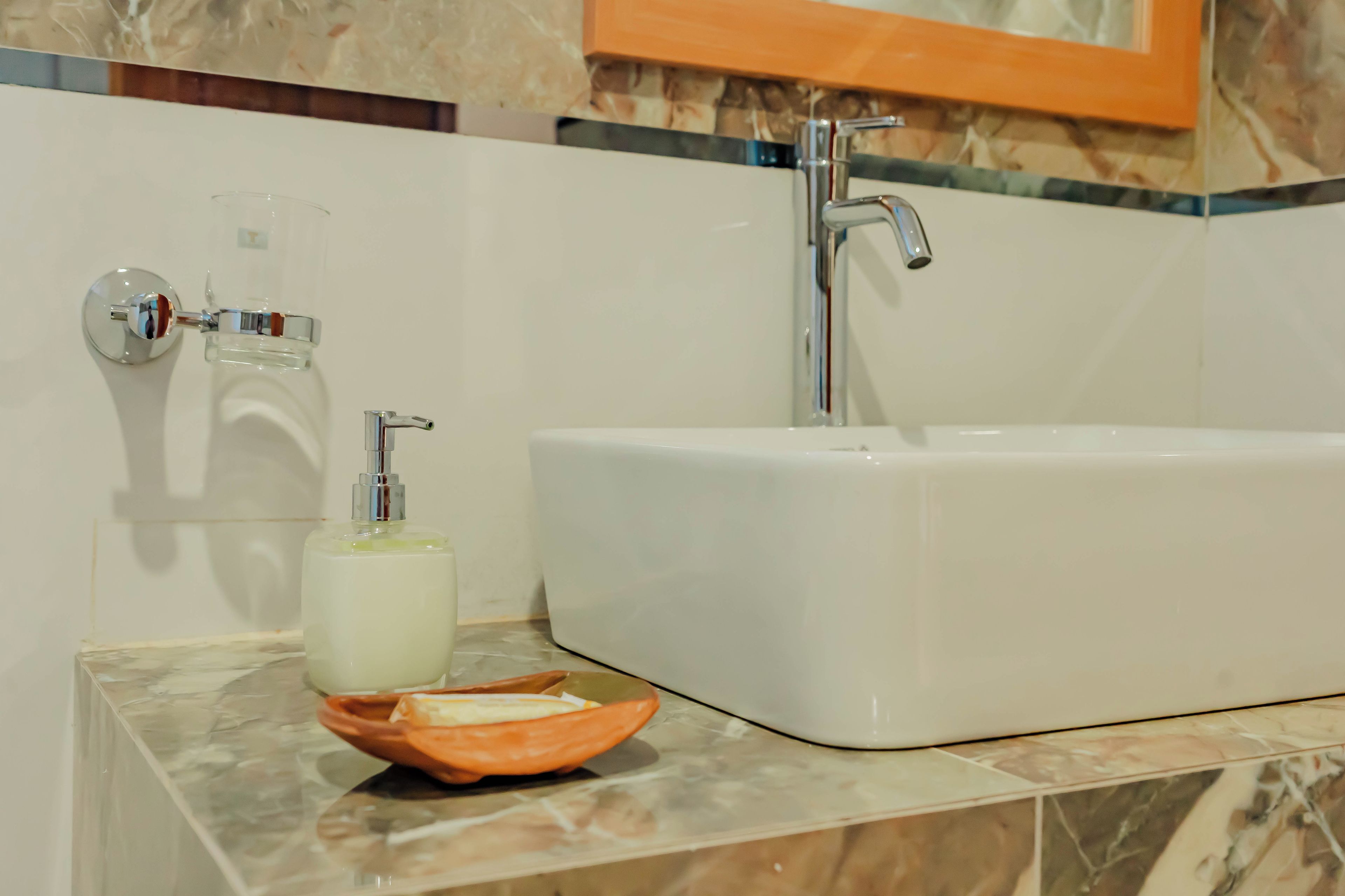 Un baño con una bañera blanca, un dispensador de jabón de vidrio y una botella de jabón sobre una encimera de mármol.