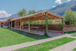 A covered outdoor seating area with tables and chairs, a brick wall, and a mountain backdrop.