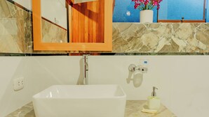 A bathroom with a rectangular sink, a mirror, a potted plant, and a soap dispenser.