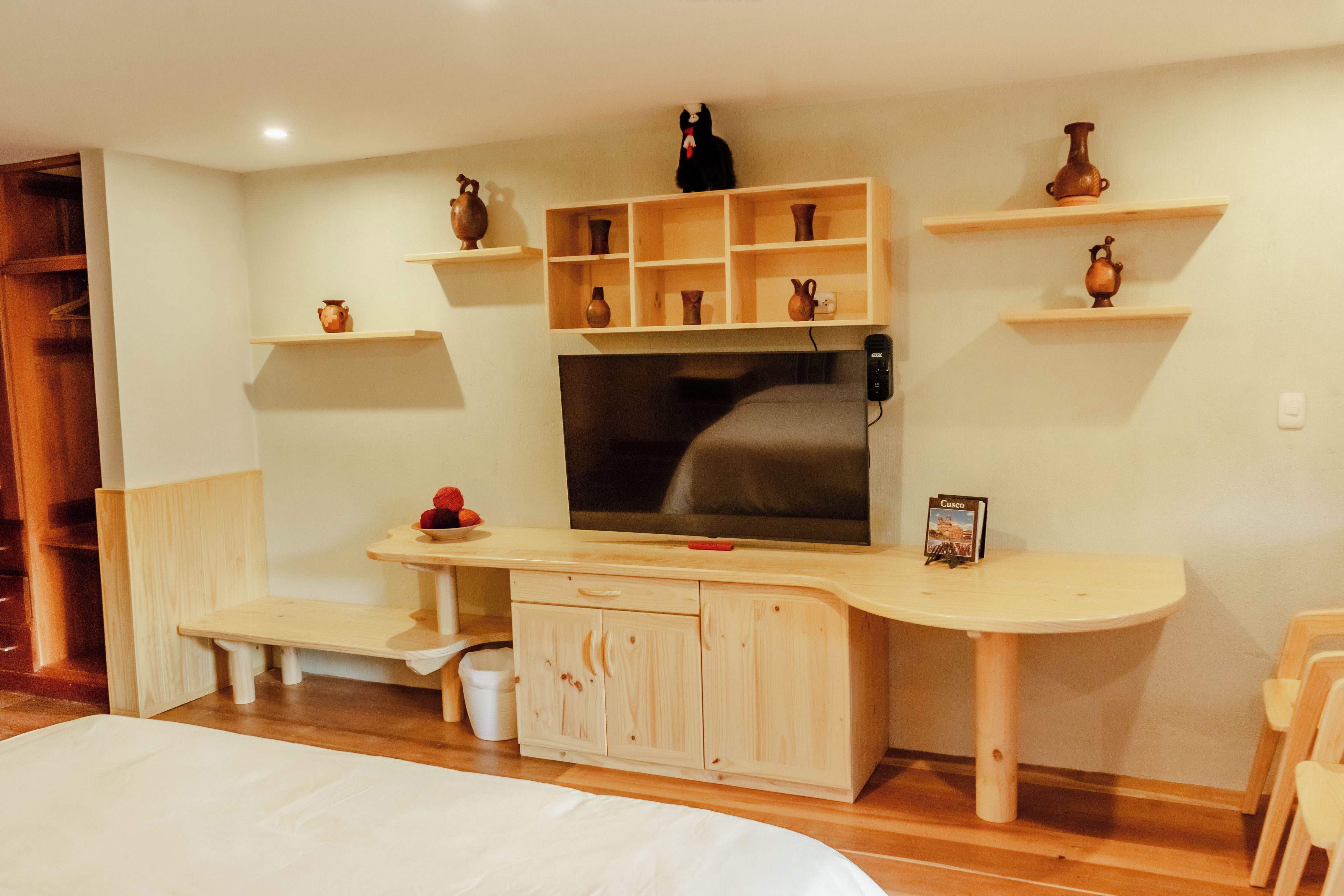 A room with a bed, a TV, wooden shelves with decorative items, and a bench.