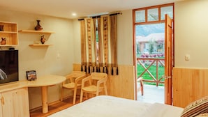 A room with a bed, a desk with chairs, a television, and a window with curtains.