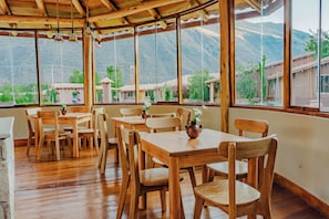 A wooden interior with tables and chairs, large windows offering a view of mountains and greenery. - CCAYPA Willka Qhichwa (Calca)