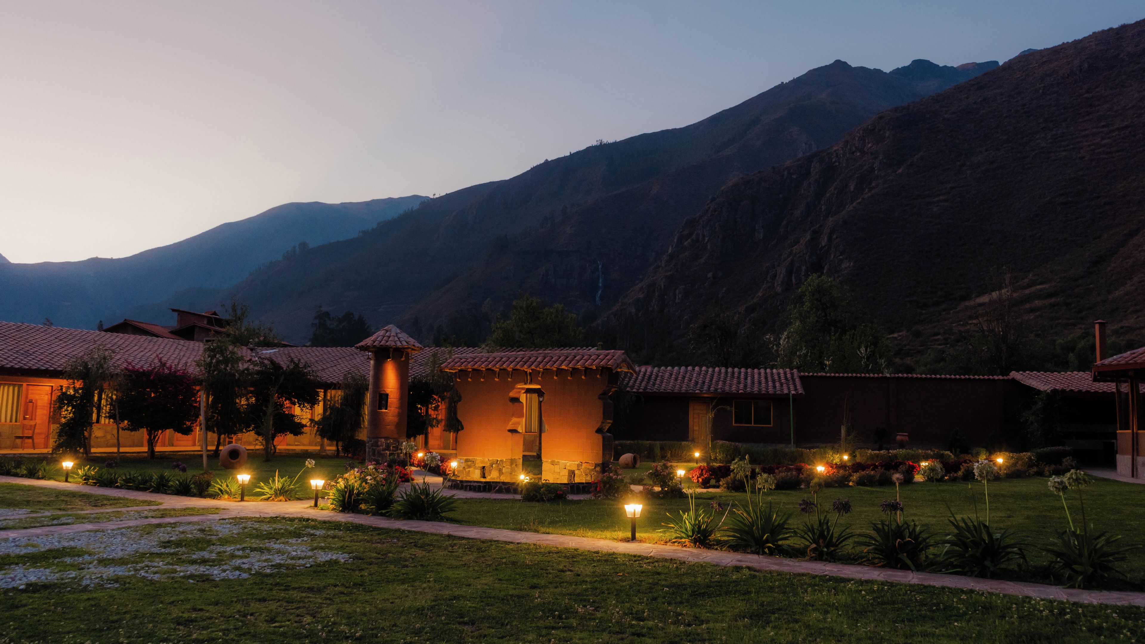 A hotel with multiple buildings, each with a red-tiled roof, set against a mountainous backdrop.