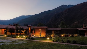 A hotel with multiple buildings, each with a red-tiled roof, set against a mountainous backdrop.