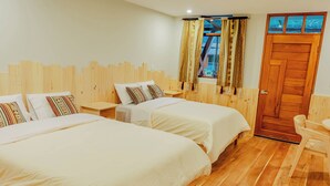 A hotel room with two beds, a wooden headboard, a window with patterned curtains, and a wooden door.
