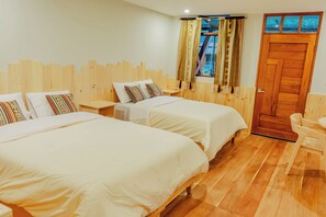A hotel room with two beds, a wooden headboard, a window with patterned curtains, and a wooden door.