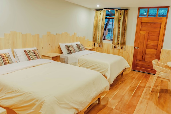 A hotel room with two beds, a wooden headboard, a window with patterned curtains, and a wooden door.