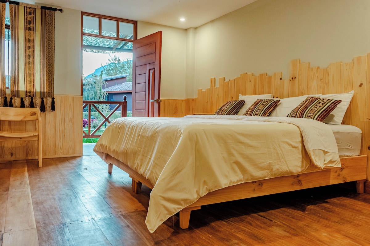 A bedroom with a wooden bed, a wooden desk, and a view of the outdoors through a window.