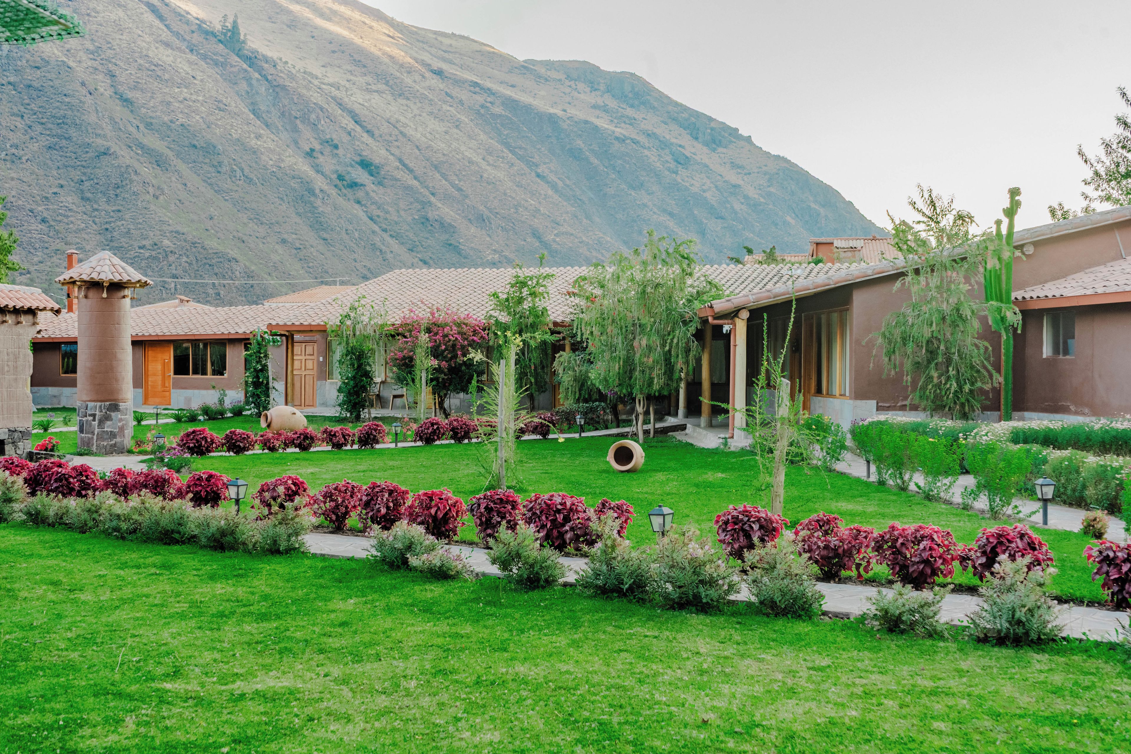 A courtyard with a mountain backdrop, featuring a building with a tiled roof and a garden with red foliage.