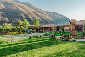 A house with a patio, surrounded by a well-maintained garden and a mountain backdrop.