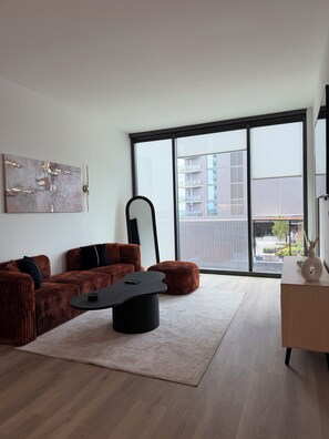 A modern living room with a sofa set, a coffee table, and a large window offering a view of a building. - Cozy 1-bedroom apartment in charming Atlanta with AC and gym access (Atlanta)