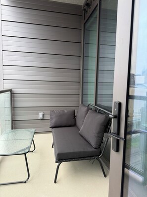 A balcony with a metal-framed sofa and a glass table, a sliding glass door, and a metal railing. - Cozy 1-bedroom apartment in charming Atlanta with AC and gym access (Atlanta)