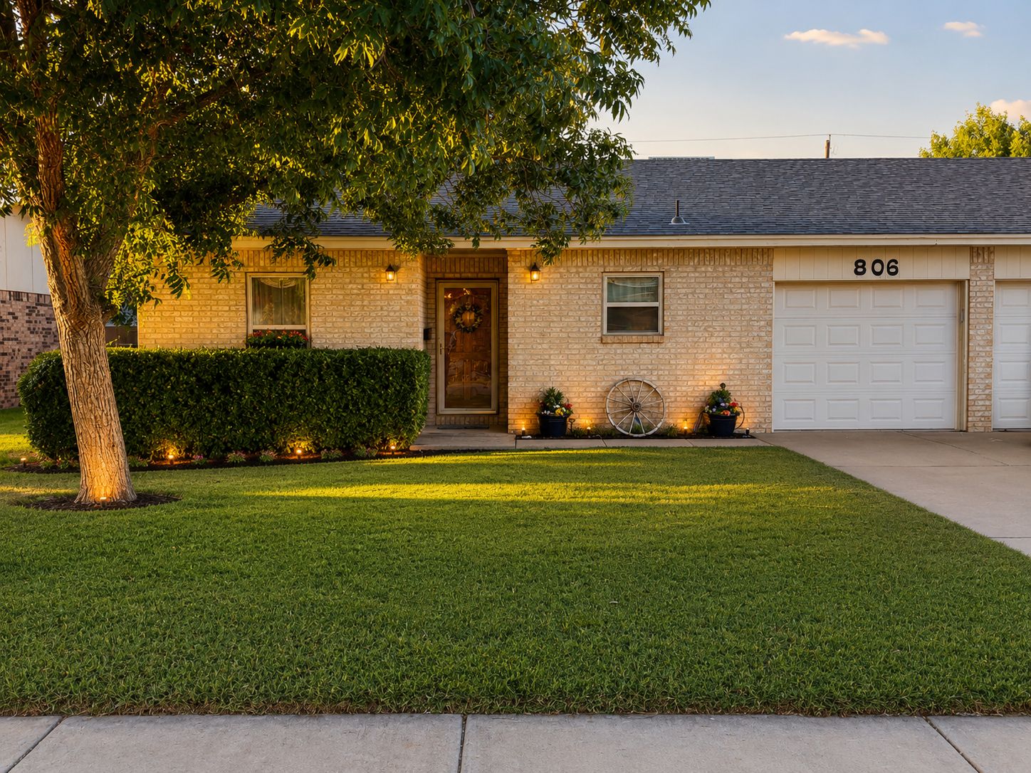 A residential house with a brick facade, a front door with a wreath, a garage with the number 806, and a well-maintained lawn.