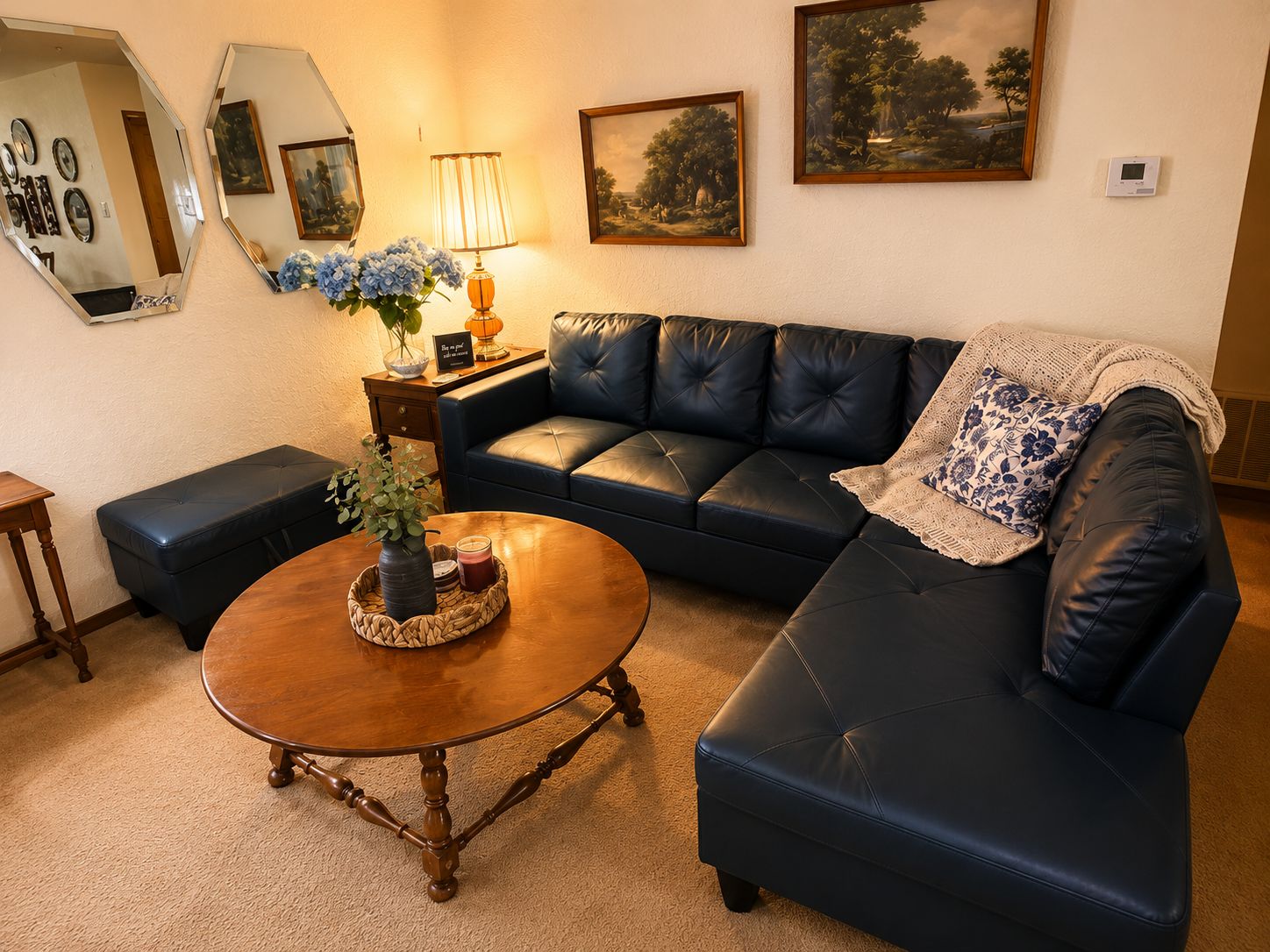 A living room with a dark leather sofa, a wooden coffee table with a vase and candle, and a lamp on a side table.