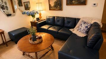 A living room with a dark leather sofa, a wooden coffee table with a vase and candle, and a lamp on a side table.