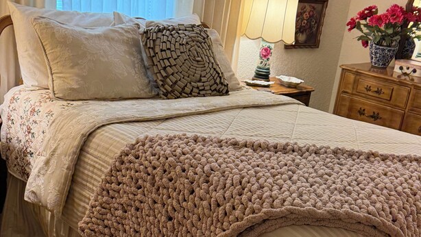 A neatly made bed with a knitted blanket, a floral bedspread, and a wooden headboard. - Vintage Charm-Modern Comfort•2BR/2BA home (Lovington)